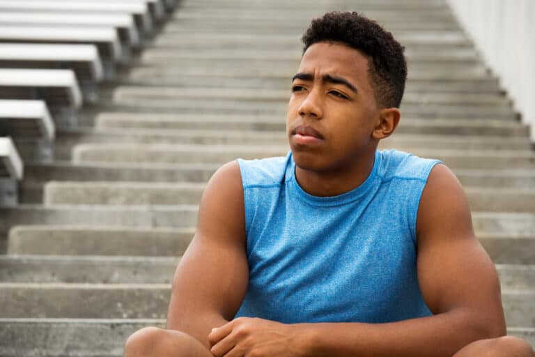 high school football recruiting featured image with a young high school athlete sitting in a football stadium thinking about his fututre